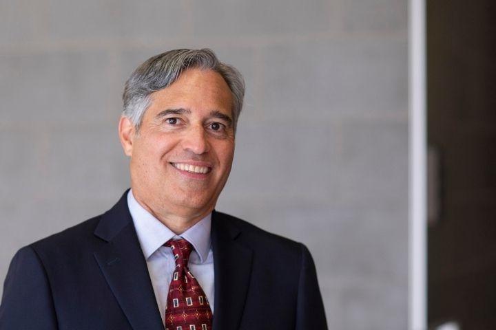 Man with gray hair with dark blue suit, red tie and light blue shirt